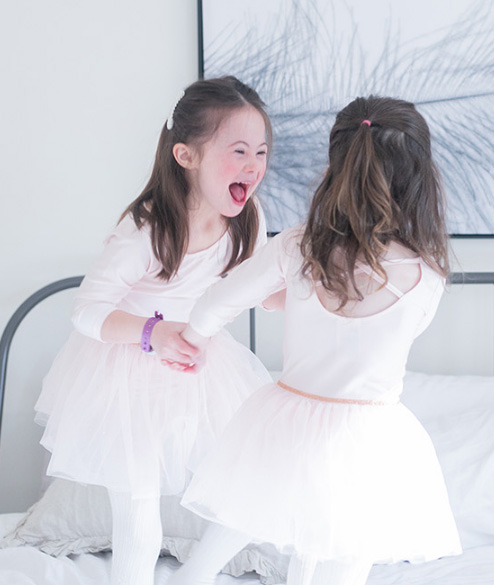 Two young girls jumping on a bed